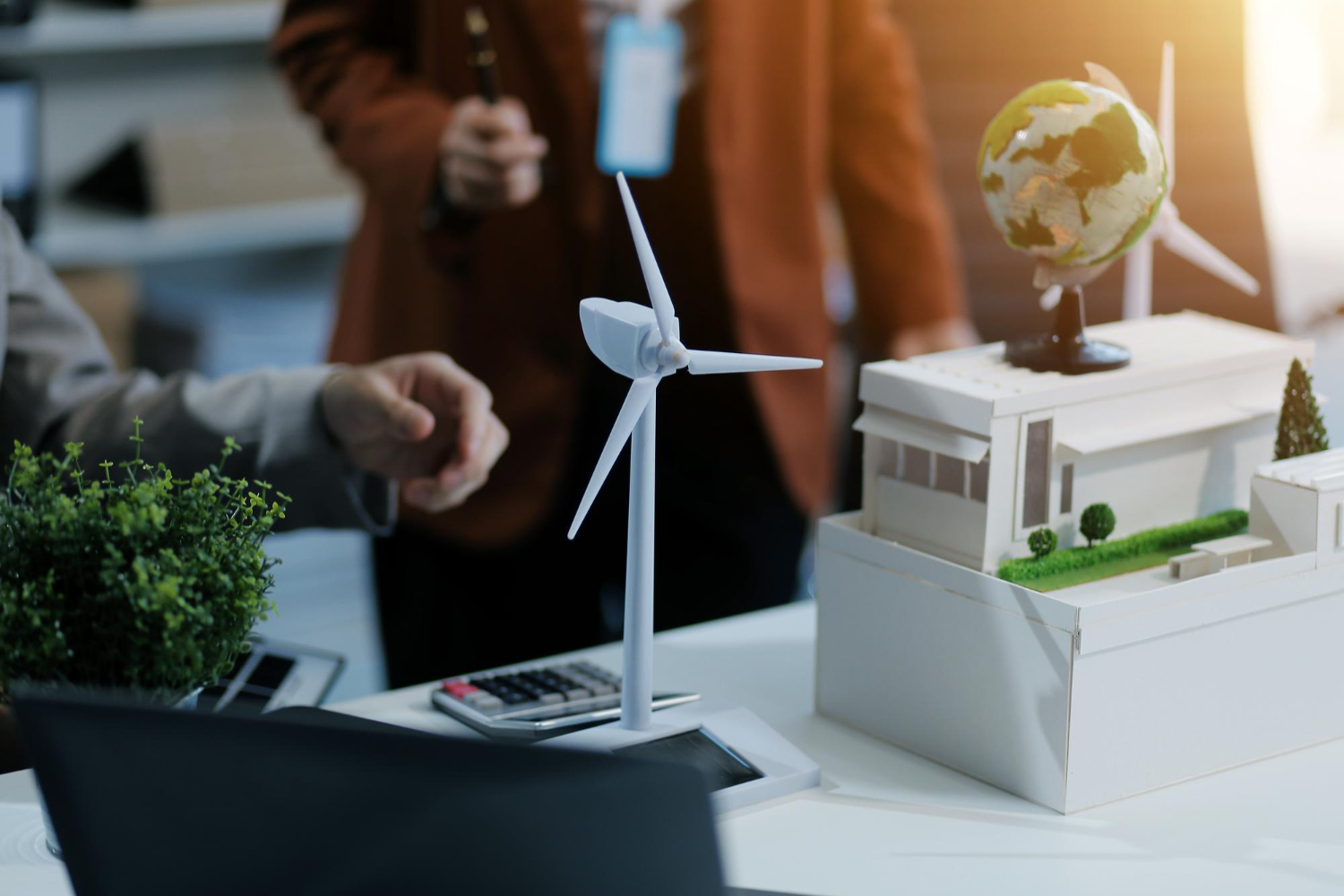 A sustainable building project model on a desk being reviewed, a scale model of a wind turbine and a home