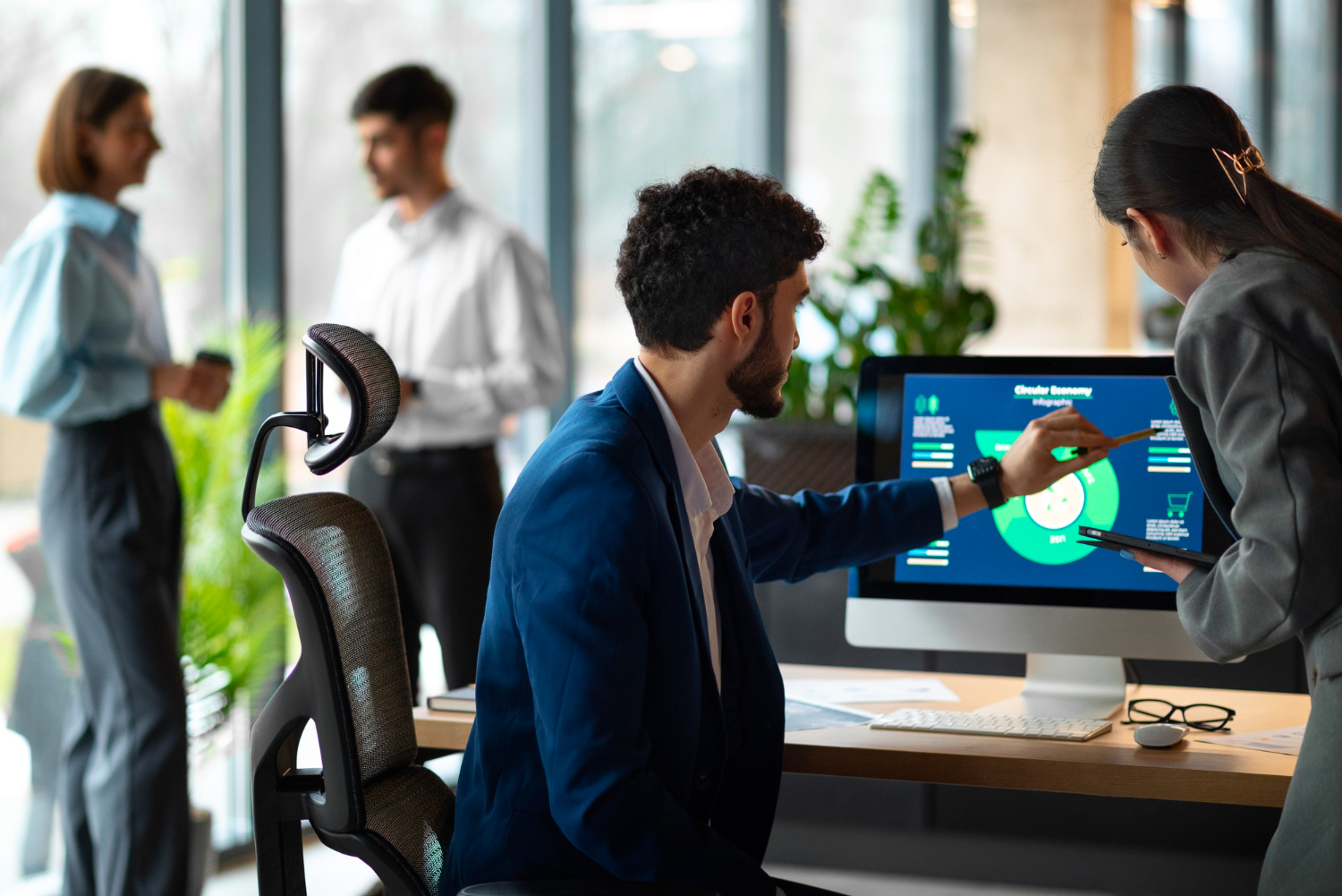 2 people stood around a desk in an office environment, 1 is pointing to a data chart and the other is looking at it with intrigue