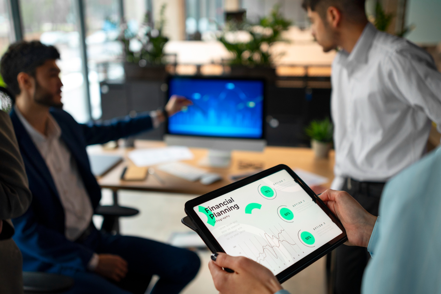 3 people standing around a desk one is holding an ipad taking notes on the governance information to create a marketing plan