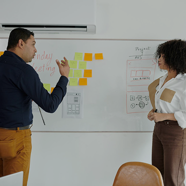 2 people stand at a white board discussing growth plans for peter and clark