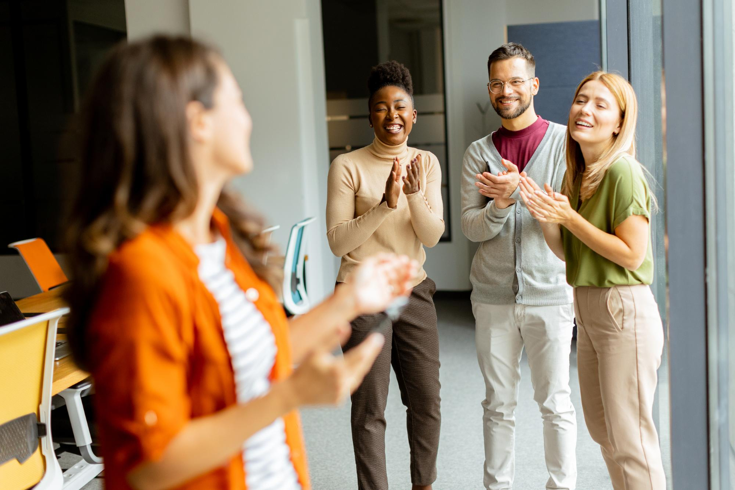 Young business woman woman standing in front of her team at the modern office. They are all smiling and clapping.